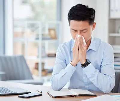 photo of a man suffering from nasal allergies and blowing his nose into a tissue.